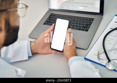 Männlicher Arzt hält Mobiltelefon in den Händen und schaut auf den weißen Mockup-Bildschirm. Stockfoto