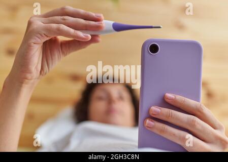 Nahaufnahme der Hände einer Frau, die ihre Basaltemperatur gemessen hat Stockfoto