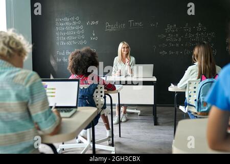 Glückliche reife Lehrerin, die Kinder in der Matheklasse in der Junior School unterrichtet. Stockfoto