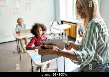 Lehrer, der Schüler in der Klasse mit einem digitalen Tablet im Klassenzimmer unterrichtet. Stockfoto