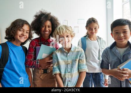 Fröhliche, vielfältige Schüler der Junior-Schule Kinder, die im Klassenzimmer auf die Kamera schauen. Stockfoto