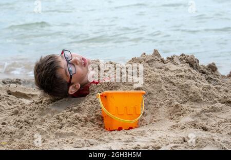 Ein kleiner Junge wird im Sand am Ufer des Lake M Michigan USA begraben Stockfoto