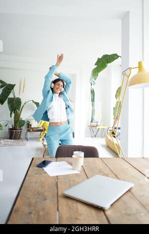 Erfolgreiche Geschäftsfrau aus Latina tanzt in Bürokleidung und feiert bei der Arbeit fröhlich. Weibliche Büroangestellte mit Kopfhörern machen die Verrückten in der Stockfoto