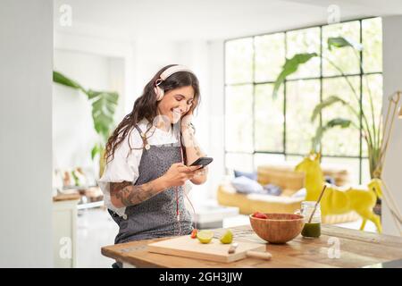 Schöne junge Frau, die mit Kopfhörern zu Hause morgens Musik hört und ein gesundes Frühstück in einer schönen Wohnung hat. Gesundes Lebensmittelkonzept. Stockfoto