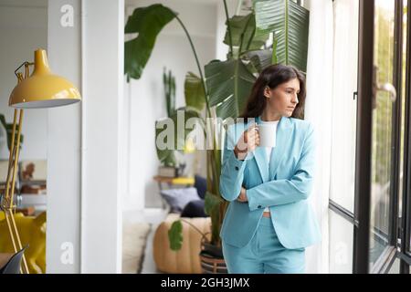 Junge Geschäftsfrau genießt es, sich bei ihrem morgendlichen Kaffee oder Tee zu entspannen und aus dem Fenster zu schauen. Schöne Latina Frau immer inspiriert auf Pause von Stockfoto
