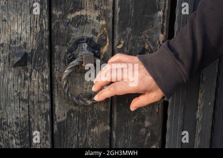 Nahaufnahme der Hand eines Mannes, der an eine alte Holztür klopft Stockfoto