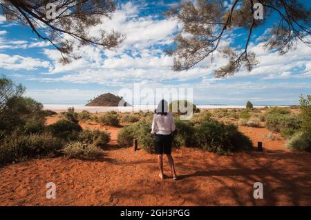 Eine weibliche Touristin, die den Lake Ballard in Westaustralien betrachtet, umrahmt von der Baumdecke des Campingplatzes mit Blick auf den großen Salzsee. Stockfoto