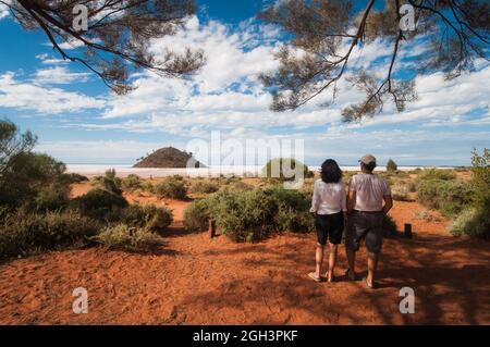 Ein männlicher und weiblicher Tourist, der den Lake Ballard in Westaustralien betrachtet, umrahmt von der Baumdecke des Camps mit Blick auf den großen Salzsee. Stockfoto