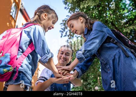 Eine junge Frau unterstützt die Töchter moralisch mit Händen ermutigt die Kinder, Mutter begleitet die Schüler zur Schule. Stockfoto