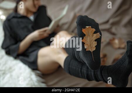 Eine Frau in warmen Strümpfen auf einem verschwommenen Hintergrund und einem Herbstblatt im Fokus. Stockfoto