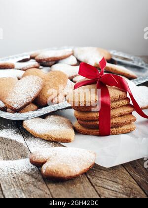 Herzförmige Shortbread-Kekse, die mit Puderzucker auf Pergamentpapier bestreut wurden. Stockfoto