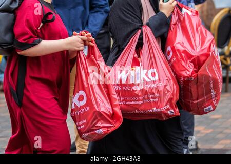 Frauen mit Red Wilko Retail Ltd Läden, Käuferinnen und Einkäufer von Plastiktüten aus recyceltem Material; wiederverwendbare, recycelbare Ladentaschen for Life, Chapel Street, Preston, Großbritannien Stockfoto