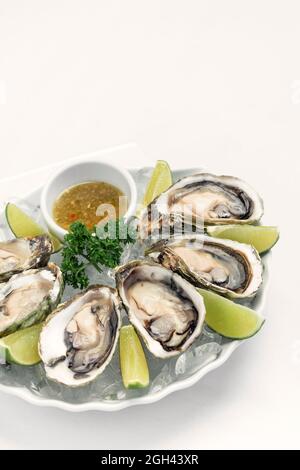Sechs frische Austern mit Limettenkeilen und Zitrusfrucht-Vinaigrette-Sauce Stockfoto