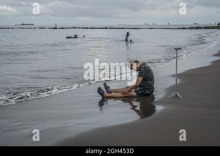 Makassar, Süd-Sulawesi, Indonesien. September 2021. Ein alter Mann sitzt auf dem Strandsand für die Gesundheitstherapie. Nach der Entspannung der Aktivitäten der Regierung während der Pandemie von Covid-19 konnten viele Bewohner Erholung und Reisen am Strand Unternehmen. (Bild: © Herwin Bahar/ZUMA Press Wire) Stockfoto