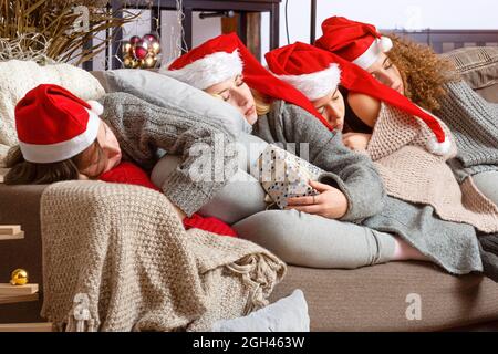 Vier junge Teenager Mädchen in roten santa Hüte eingeschlafen Auf der Couch nach dem Einwickeln von Weihnachtsgeschenken Stockfoto