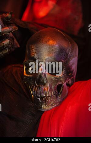 Halloween-Dekorationen, gruselige gruselige furchterregende schreckliche Totenkopf Maske in blutigen rot-orange-goldenen Farben in der Nähe der Hand des Hexenmörders in Lumpen mit Metallfingern Stockfoto