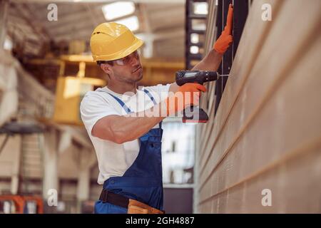 Schöner männlicher Arbeiter, der auf der Baustelle Bohrmaschine benutzt Stockfoto