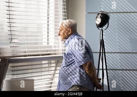 Nachdenklicher trauriger älterer 80er-Jahre-Mann, der aus dem Fenster schaute Stockfoto