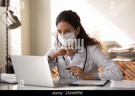 Junge Hausarzt in medizinischen Gesichtsmaske arbeiten am Laptop Stockfoto