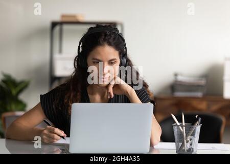 Fokussierte Erwachsene Studentin in Kopfhörern mit Laptop Stockfoto