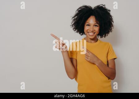 Fröhliche dunkelhäutige Frau in gelbem T-Shirt mit Zeigefinger in der linken oberen Ecke Stockfoto