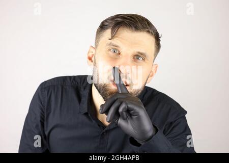 Ein Mann mit medizinischen Handschuhen legt seinen Zeigefinger auf seine Lippen und macht eine stille Geste Stockfoto