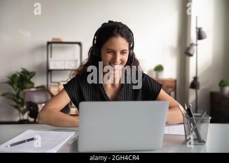Glückliche, tausendjährige Geschäftsfrau im Headset, die am Laptop arbeitet Stockfoto