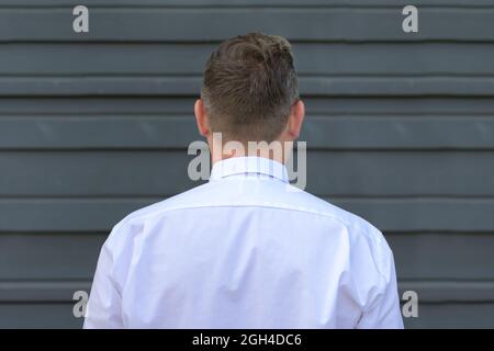 Kopf- und Schulteransicht eines Mannes in weißem Langarm-Hemd, der vor einer grauen Außenwand steht Stockfoto