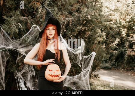 Halloween Hexe Rotschopf Frau macht Hexerei mit magischen Buch der Zaubersprüche, Magie in ihren Händen. Schöne junge Frau in Hexenhut beschwörend. Gruselig Stockfoto