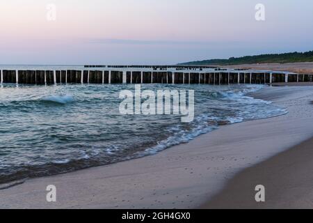 Sonnenaufgang am frühen Morgen, der durch die Wolken platzt. Gezeiten im Morgengrauen. Wellen schlagen den Meeresschaum auf dem Sand am Strand Stockfoto