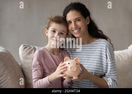 Lächelnde junge Mutter und kleines Kind halten ein Sparschwein. Stockfoto