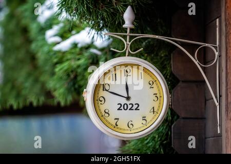 Vintage-Straßenuhr an der Wand eines Holzgebäudes zeigt die Uhr, dass es nur noch wenige Minuten bis zum 2022, Neujahr-Konzept gibt Stockfoto