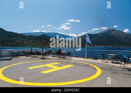 Poros, Insel Cefalonia, Griechenland - Juli 17 2019: Gelbes Helipad-Zeichen für Hubschrauber auf dem Schiff und Passagiere, die sich am offenen Deck entspannen. Fähre von der Insel Cefalonia. Stockfoto