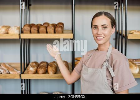 Porträt einer positiven jungen Frau in Schürze, die mit Brot und Brot in der Brotauswahl steht Stockfoto