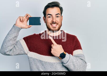 Hübscher kaukasischer Mann mit Bart, der SSD-Speicher hält, lächelt glücklich und zeigt mit Hand und Finger Stockfoto