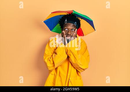 Junger afroamerikanischer Mann mit gelbem Regenmantel müde Hände, die Gesicht, Depression und Traurigkeit bedecken, aufgeregt und wegen des Problems verärgert Stockfoto