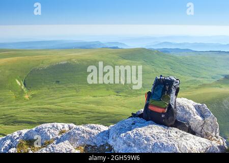 Der Rucksack liegt auf den Felsen in den Bergen vor dem Hintergrund eines Feldes Stockfoto