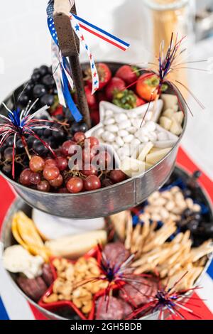 Am 4. Juli gab es ein Charcuterie-Brett auf einem zweistufigen Metallständer, gefüllt mit Käse, Crackern, Salami und frischem Obst Stockfoto