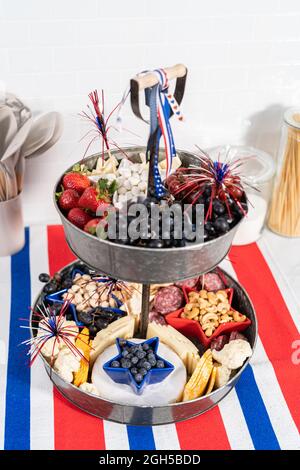 Am 4. Juli gab es ein Charcuterie-Brett auf einem zweistufigen Metallständer, gefüllt mit Käse, Crackern, Salami und frischem Obst Stockfoto