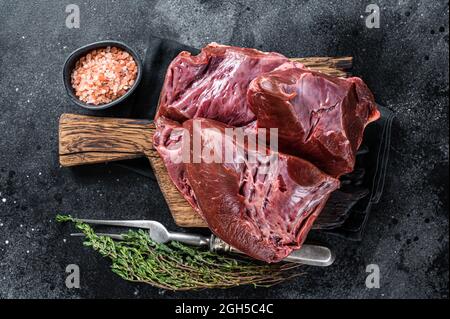 Rohes geschnittes Rind- oder Kalbsherz auf einem Schlachtbrett. Schwarzer Hintergrund. Draufsicht Stockfoto