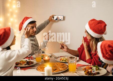 Glückliche Familie, die während des veganen Abendessens mit der älteren Großmutter eine Weihnachts-Videoanruferparty auf dem Handy macht – konzentrieren Sie sich auf das Gesicht der Mutter Stockfoto