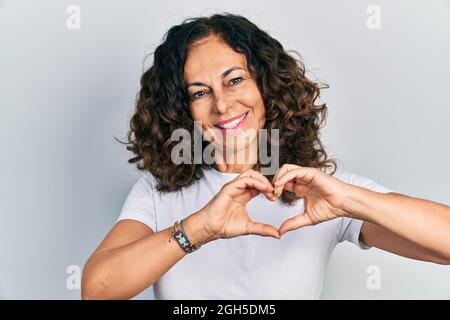 Mittelalter hispanische Frau trägt lässige weiße T-Shirt lächelnd in Liebe tun Herz Symbol Form mit Händen. Romantisches Konzept. Stockfoto