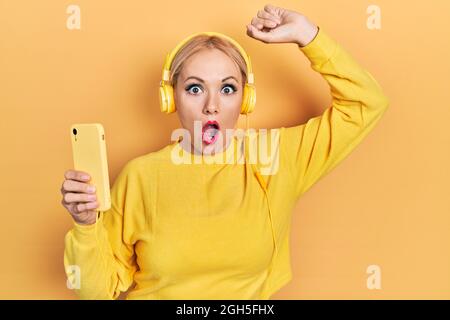 Junge blonde Frau, die mit Kopfhörern tanzt, ängstlich und schockiert von Überraschung und staunendem Ausdruck, Angst und aufgeregtes Gesicht. Stockfoto