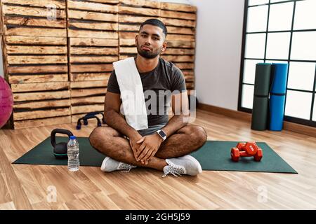 Junger indischer Mann, der im Fitnessstudio auf einer Trainingsmatte sitzt, ist depressiv und sorgt sich um Not, weint wütend und ängstlich. Trauriger Ausdruck. Stockfoto