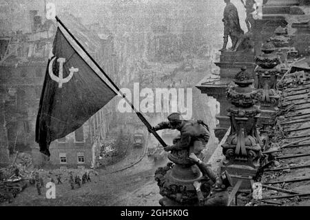 Ein sowjetischer Soldat, der die kommunistische Rote Flagge auf dem Reichstag in Berlin aufhebt, April 1945. Dies ist das ungedoktorte Foto - die Männer haben eine Uhr an jedem Handgelenk. In späteren Versionen, die von der sowjetischen Regierung zensiert wurden, wurden diese gestohlenen Uhren vom Foto entfernt. Stockfoto