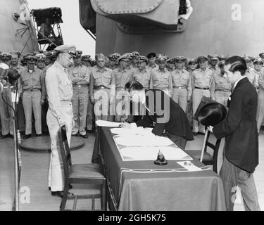 Der japanische Außenminister Mamoru Shigemitsu unterschreibt am 2. September 1945 das Instrument der Kapitulation an Bord der USS Missouri. Lieutentant General Richard K. Sutherland, U.S. Army, beobachtet von der gegenüberliegenden Seite des Tisches. Stockfoto