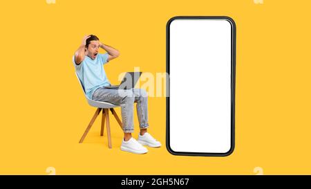Überrascht schockiert Kerl mit Laptop, leerer Telefonbildschirm Stockfoto