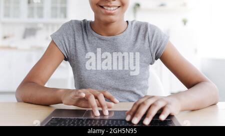 Lächelndes afroamerikanisches Mädchen, das auf der Tastatur tippt und im Inneren des Hauses am Laptop studiert Stockfoto