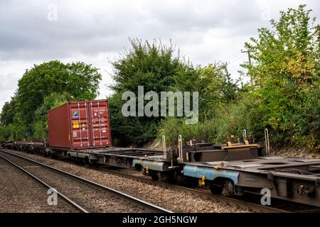 Ein Container auf meist leeren Flachbett-Eisenbahnwaggons in Richtung Hafen Felixstowe, Westerfield, Suffolk, Großbritannien. Stockfoto