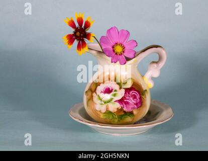 Ein zierlicher Strauß von bunten Gartenblumen in einer kleinen Vase auf einem schlichten Hintergrund. Stockfoto